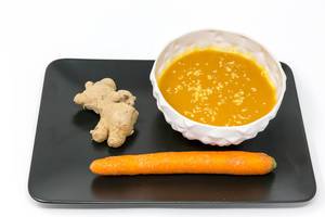 A pumpkin-coconut-cremesoup with fresh grated ginger in a bowl on a black plate with a corrat and a ginger root