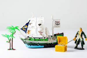 A tiny toy pirate ship with a treasure chest and a statue of a pirate on white background