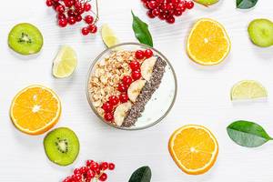 A top view of a bowl of oatmeal on a white wooden background with fresh fruits and berries