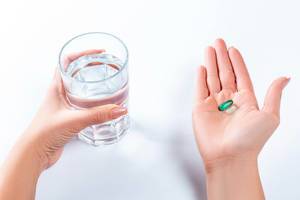 A woman holds a glass of water in one hand and a pill in the other
