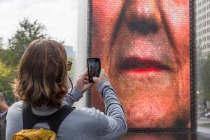 A woman photographs with her smartphone one of the faces shown on the Crown Fountain in Chicago