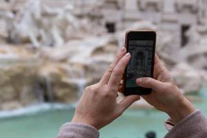 A woman takes a vertical photo with her iPhone at the Palazzo Venezia Garden in Rome