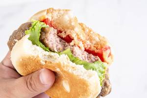 Abgebissener Hamburger in der Hand, mit Tomaten, Salat und heller Burgersoße