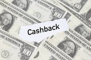 Abgerissener Notizzettel mit dem Text "Cashback" (Rückzahlung), liegt auf ausgebreiteten Dollarscheinen aus Amerika