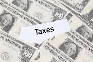 Abgerissener Notizzettel mit dem Wort "Taxes" (Steuern) auf amerikanischen Dollarscheinen