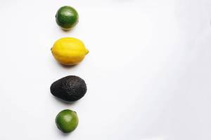 Abstrakte Aufnahme von tropischen Früchten: Zitrone, Limetten und Avocado vor weißem Hintergrund