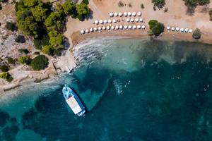 Aerial picture of a a ferry boat that docks in the argolic gulf, next to tourists at Zogeria Beach, Spetses
