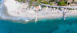 Aerial picture of empty sun chairs at Kaiki Beach, Spetses, with small waves at the island shore