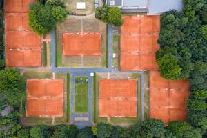 Aerial shot of several orange tennis courts, surrounded by forrest, in Cologne - Müngersdorf