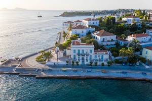 Aerial view of a coastal path & Church at Agios Mamas Beach, next to aristocratic villas on the Mediterranean island Spetses, Greece, in the Saronic Gulf