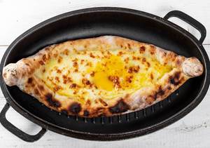 Ajarian open khachapuri with chicken egg and cheese in a black pan with white wooden background