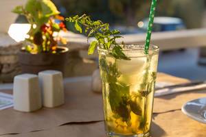 Alcoholic Drink Mojito, with fresh mint leaves, ice cubes and green straw, on an outside table under the sun