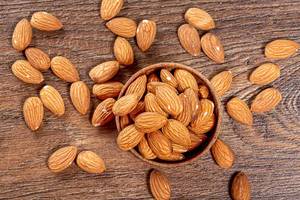 Almond nuts in wooden bowl on brown wooden background. Top view