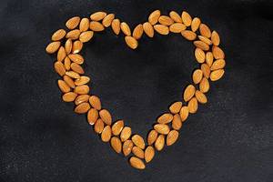 Almond nuts on a black background lined in the shape of a heart. Top view