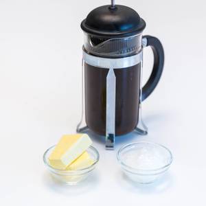 Alternative coffee machine in a glas pot with French press system, next to two bowls with butter and ice