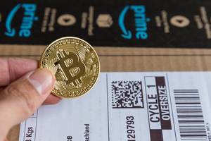 Amazon now gives the option for Bitcoin payment - Hand shows gold-colored coin with Bitcoin-logo in close-up
