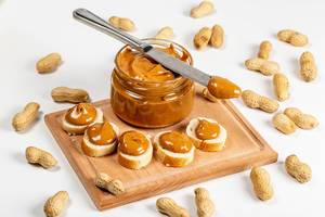 An open jar of peanut butter with sandwiches and peanuts