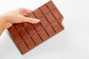 Angebissene große Tafel Milchschokolade in einer Frauenhand