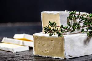 Angeschnittener Brie-Käse mit frischem Thymian vor schwarzem Hintergrund