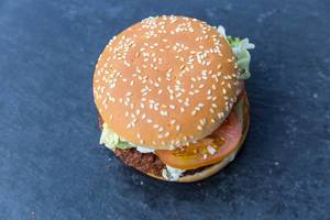 Ansicht von oben auf den Fleischersatz - Burger "Big Vegan TS" im Sesam-Burgerbrötchen, mit grünem Blattsalat, Senfsoße, Sojabratling, auf dunklem Tisch