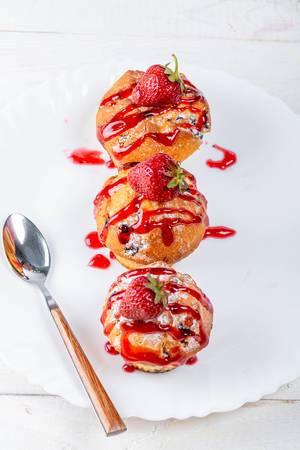 Ansicht von oben auf Erdbeeren-Muffins mit süßer Erdbeersoße, auf einem weißen Teller neben einem Löffel