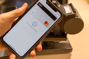 Apple Pay auf in der Hand gehaltenem Smartphone vor Kasse