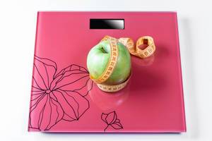Apple wrapped with measuring tape on the scales as a symbol of a healthy diet