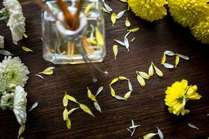 AROMA geschrieben aus gelben Blütenblättern auf  dunkelbraunem Holztisch mit Duftstäbchen