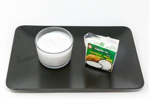 Aroy D - Coconut Milk in glas with packaging on black plate