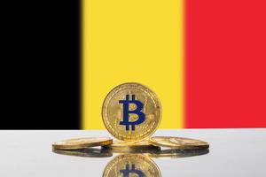 Arrangement aus vier goldenen Bitcoin-Münzen vor der dreifarbigen Flagge des Landes Belgien