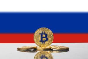 Arrangement aus vier goldenen Bitcoin-Münzen vor der russischen Flagge