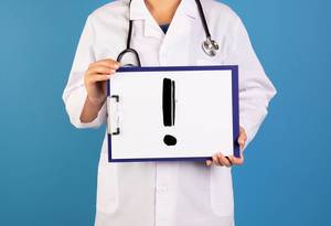 Arzt hält ein Schild mit einem Ausrufezeichen im blauen Hintergrund
