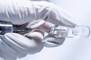 Arzt mit Handschuhen zieht Spritze an Ampulle auf und bereitet Injektion vor