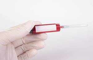 Arzthand hält eine Blutspritze mit Injektionsnadel und freier Fläche für Text