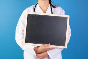 Ärztin im blauen Hintergrund hält eine schwarze Tafel in der Hand