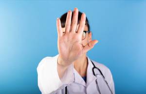 Ärztin zeigt Stop mit der Hand vor einem blauen Hintergrund