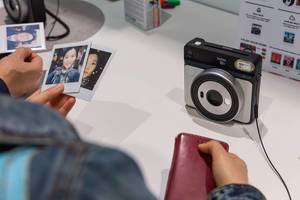 Asiatische Frau hält Ausdruck von Fotos der Sofortbildkamera Instax Square SQ6 an der Photokina in Köln