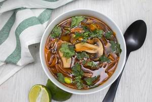 Asiatische Suppe mit verschiedenen Pilzen, Bambussprossen und Petersilie neben Limette