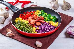 Asparagus, Brussels sprouts, corn, peppers and sausages in a frying pan