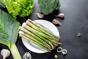 Asparagus, lettuce, broccoli, leeks and garlic on black background. Top view (Flip 2019)