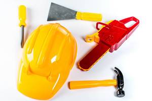 Assorted plastic toy tools and yellow helmet over white background