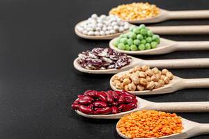 Assortment of legumes in wooden spoons on black background (Flip 2019)