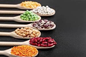 Assortment of legumes in wooden spoons on black background
