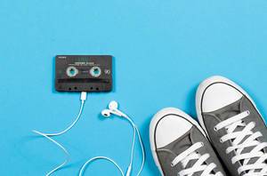 Audio Cassette with headphones and sneakers on blue background
