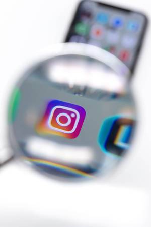 Auf Mobiltelefon installierte Instagram App durch Lupe betrachtet vor weißem Hintergrund