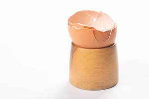 Aufgebrochene leere Eierschale in hölzernem Eierbecher vor weißem Hintergrund