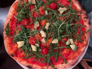 Aufnahme von oben: vegane Pizza ohne Käse und mit Tomatensauce, Avocado, Rucola und Cherrytomaten