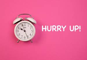 Aufschrift "Hurry Up!" - Beeile dich!,  neben einem weißen Vintage-Wecker, auf pink-blauem Hintergrund