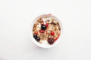 Aufsicht - Gesundes Frühstück - Joghurt mit Müsli und Waldfrüchten auf weißem Hintergrund