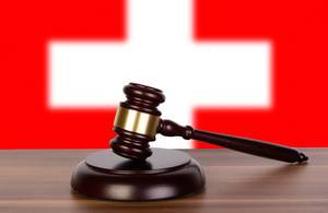 Auktionshammer / Richterhammer auf einem Holzuntergrund, vor der Flagge der Schweiz